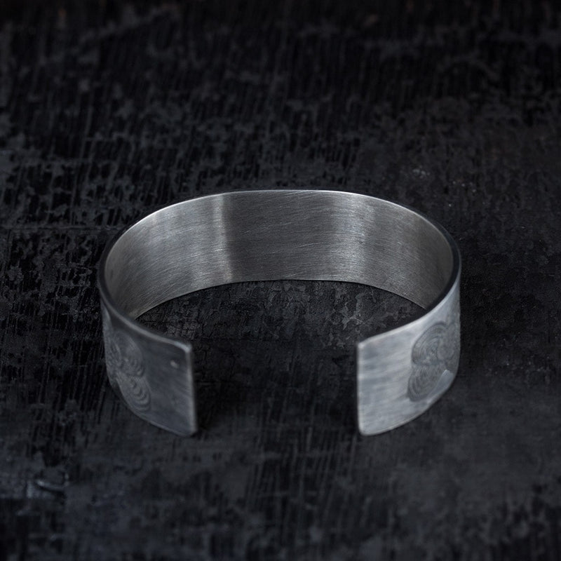 back view of a wide silver bracelet with engraved design