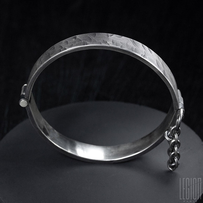 side view of a rigid black silver bracelet with a pin