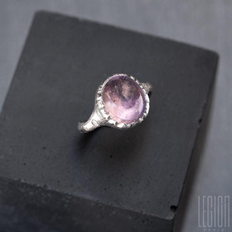 side view of a textured white gold horse ring with a white diamond on the side and a large translucent purple oval center stone