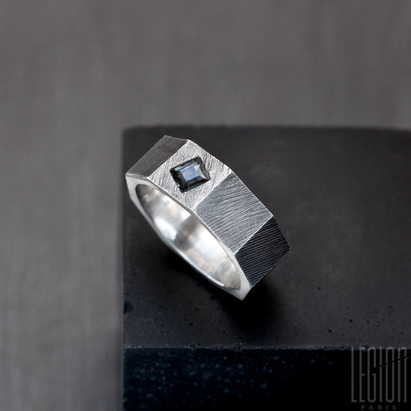 Side view of a black silver nut-shaped ring with a square blue gray stone. The ring is grooved. 