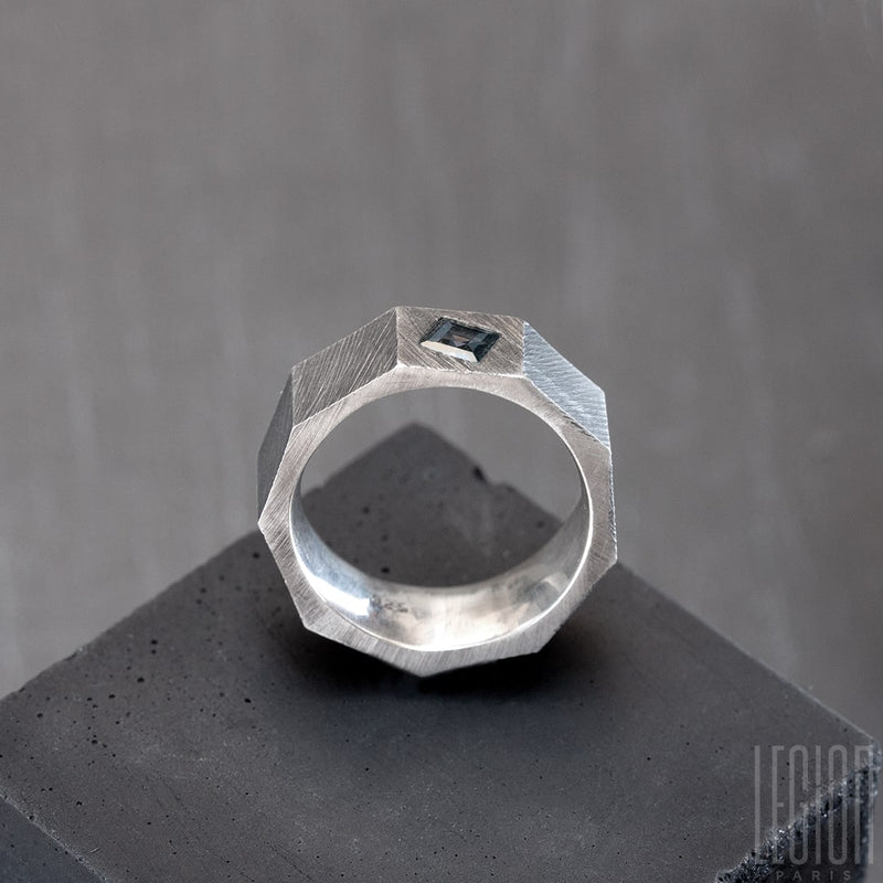 Side view of a black silver nut-shaped ring with a square blue gray stone. The ring is grooved. 