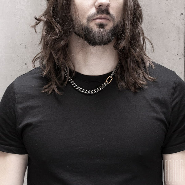 long-haired man wearing a black tee shirt and a black silver and red gold necklace with a large chain bracelet