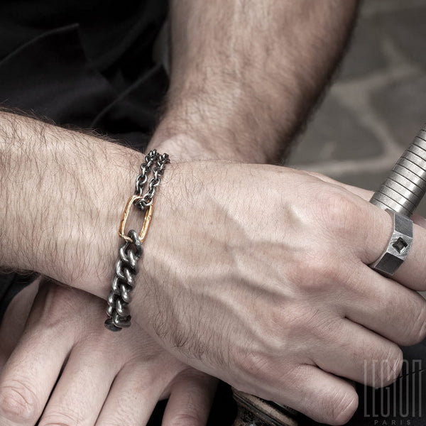 man's wrist wearing a black silver and red gold chain bracelet and a black silver signet ring