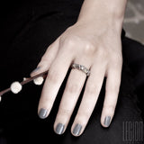Woman's hand with gray nails wearing a white gold textured ring with small sparkling stones scattered on top.