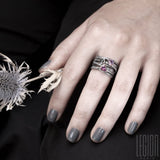 Woman's hand wearing a large Chevalière with textured and interlocking black silver twigs and 3 stones on top. A pink triangle spinel, a round blue tourmaline, both set in white gold, and an oval purple tourmaline set in claws in a red gold shawl