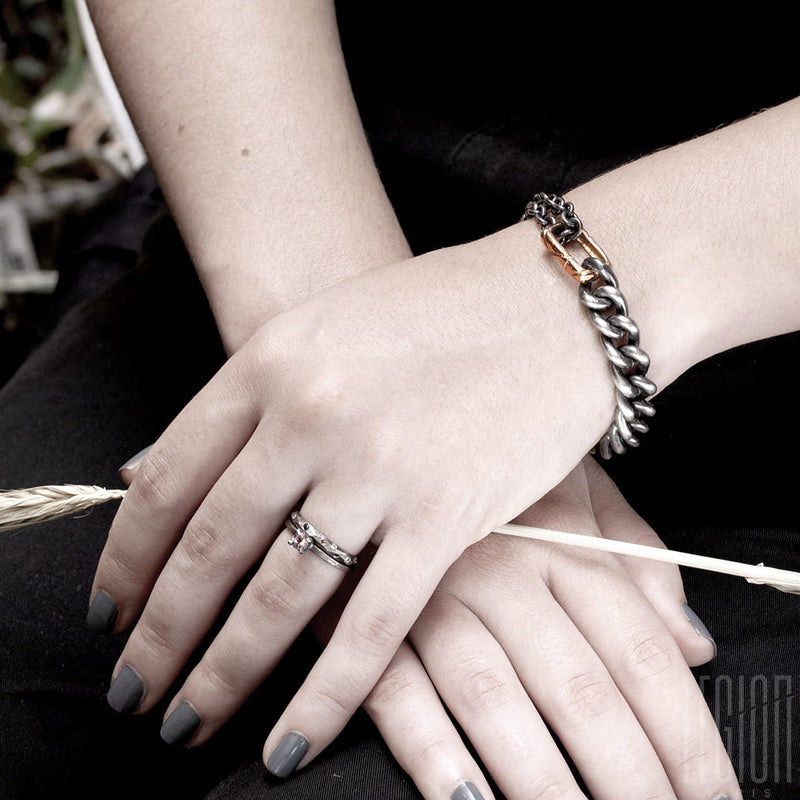 woman's wrist wearing a black silver and red gold bracelet and a white gold wedding ring with a white diamond