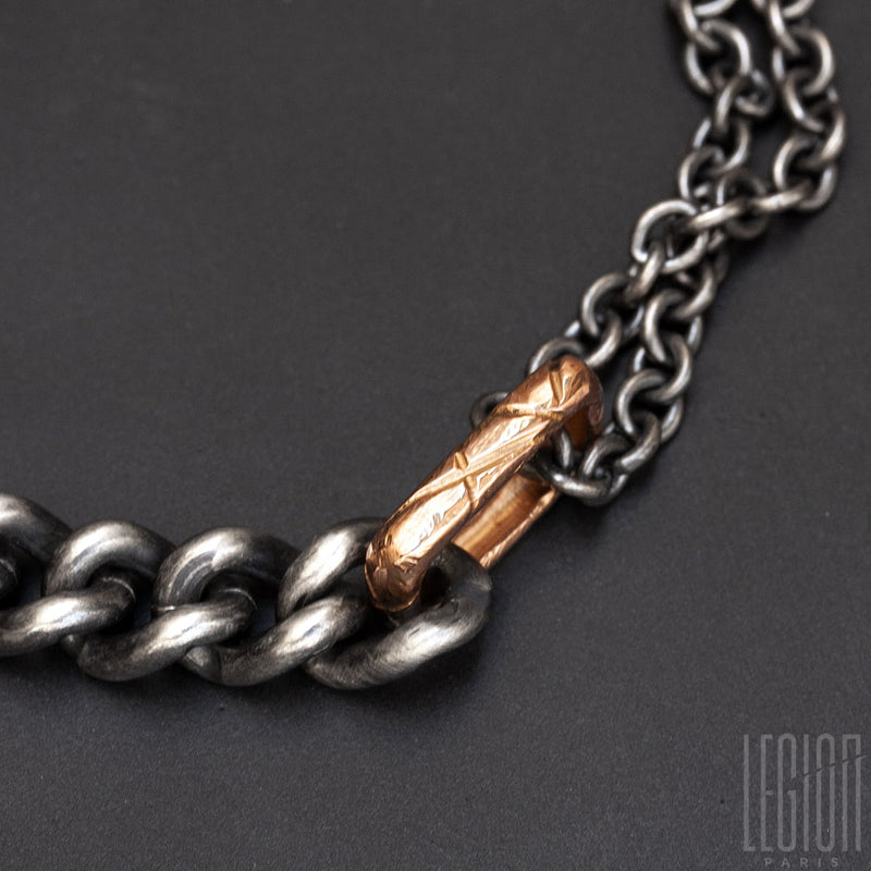close-up of a hammered and textured red gold ring with a massive black silver chain and a thinner round forçat chain