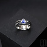 a black textured silver ring with 3 twigs crossing on top and a blue triangular tanzanite set in a closed setting with grey diamonds scattered on the ring body 