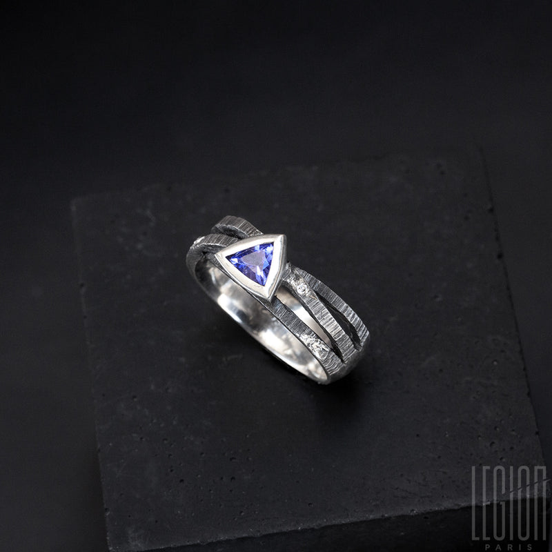 a black textured silver ring with 3 twigs crossing on top and a blue triangular tanzanite set in a closed setting with grey diamonds scattered on the ring body 