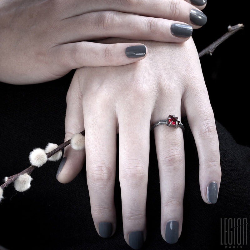 woman's hands wearing a solitaire ring with a red garnet stone