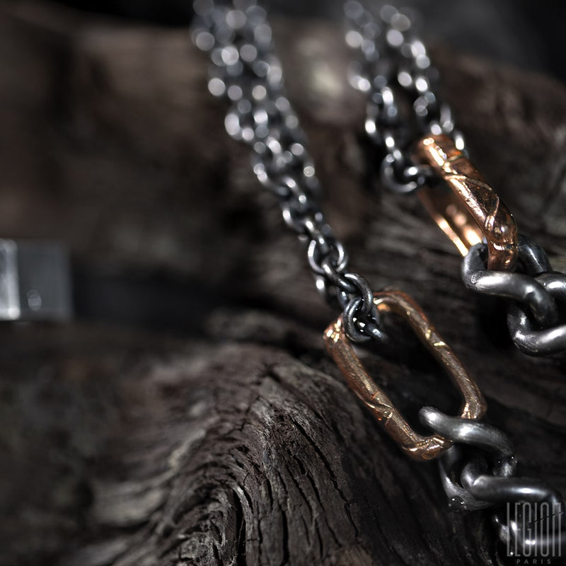 Close-up on the hammered and textured red gold link, forged with the two black silver chains that go through it. 