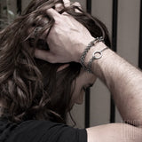 man with long hair hands on the head wearing black silver bracelets in chain