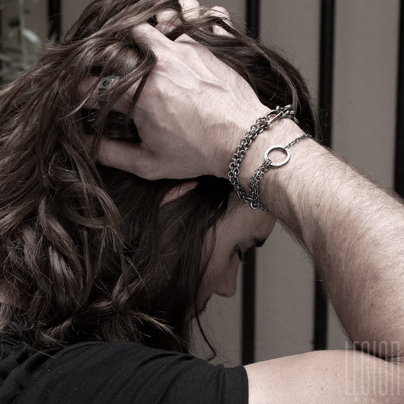 long-haired man wearing a tee shirt with two black silver bracelets on his wrist