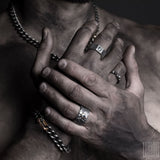hands of man wearing an assortment of black silver jewelry with chains gourmettes, rings with stones