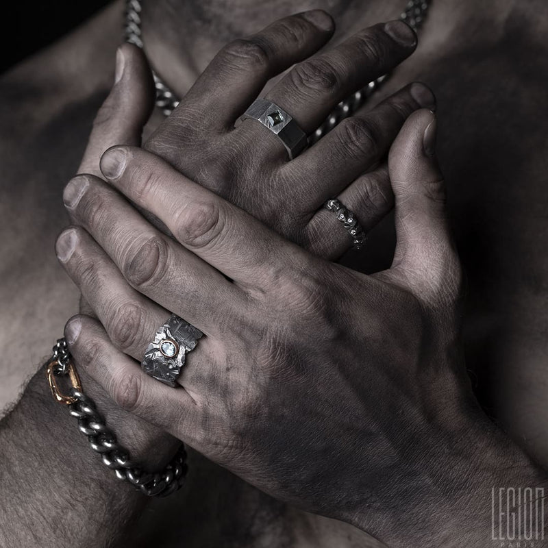 hands of man wearing an assortment of black silver jewelry with chains gourmettes, rings with stones