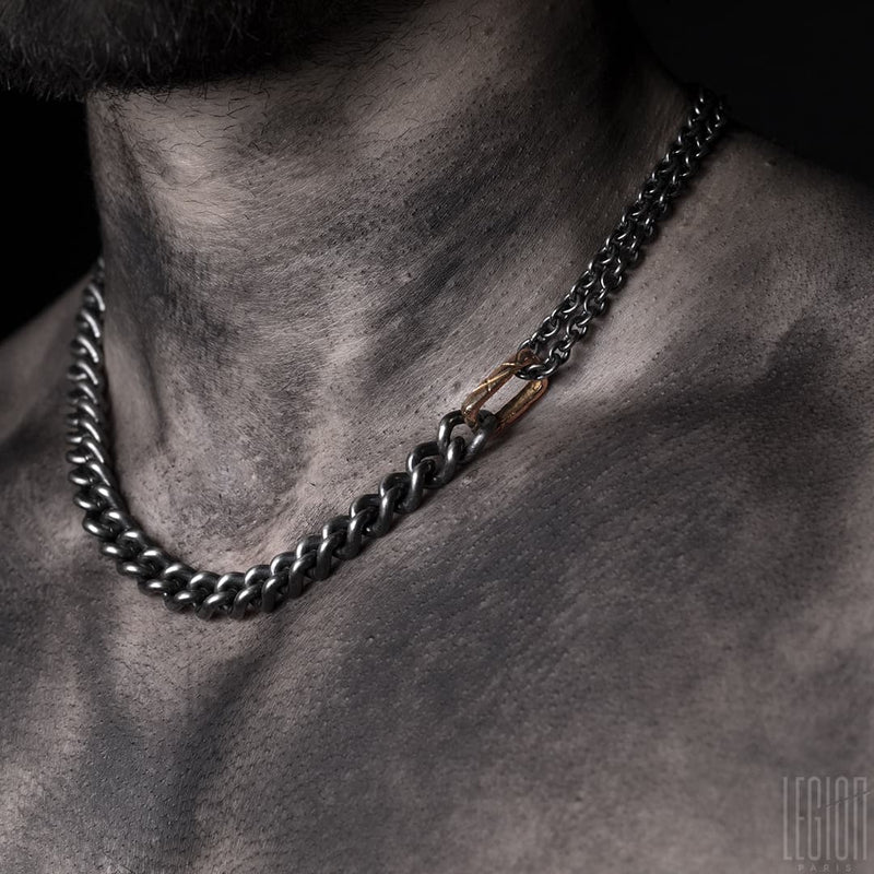 neck of shirtless man wearing a black silver necklace made from a curb chain with a hammered red gold link