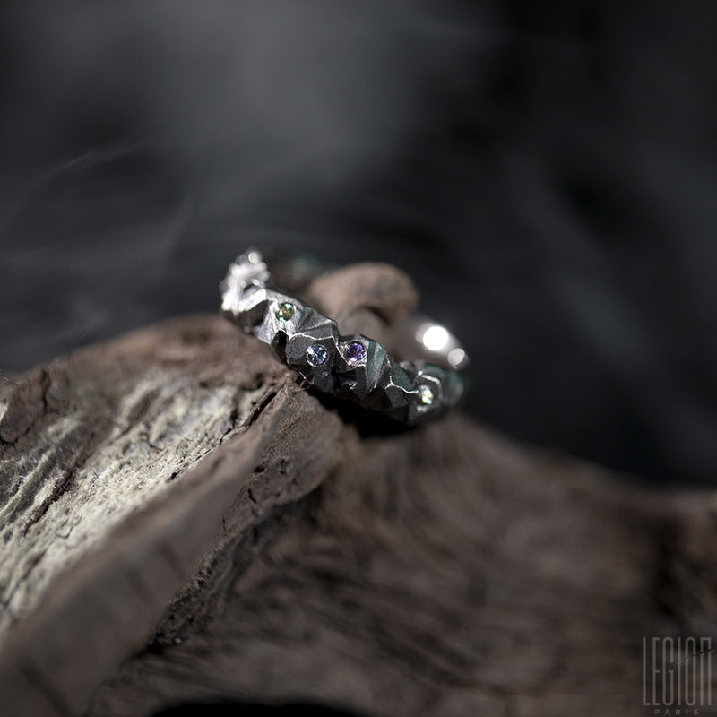 White gold ring placed on a root. On the ring small diamonds of different colors are set and scattered on it. 