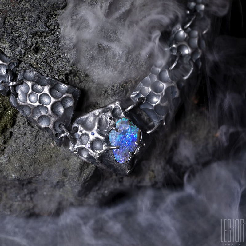 a black silver plastron necklace made of different textured black silver tiles with a raw black opal in the center